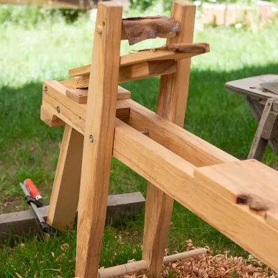A shave horse with wood shavings littering the grass around it. 