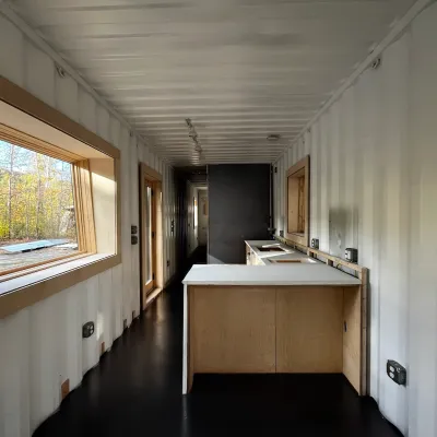  A interior of a 40-foot shipping container home featuring light wood-trimmed windows, sleek black flooring, and custom cabinetry with white concrete countertops.