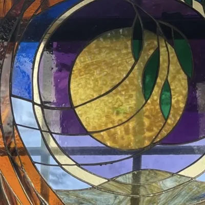 Close up shot of a stained glass panel with moon, tree, and leaves.