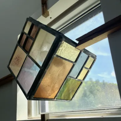 A stained glass cube hangs in a window