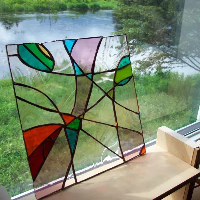 A stained glass panel sits on a windowsill in front of a view out to the pond.