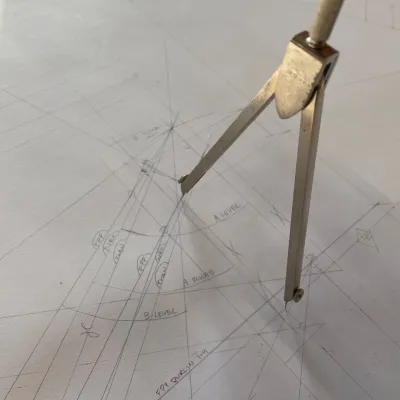 A compass poised on a piece of paper. There is complex geometry drawn on the paper.