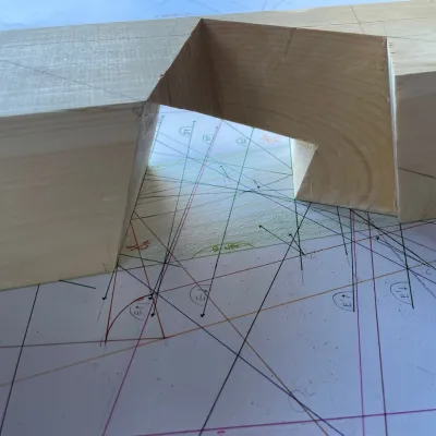 A piece of lumber with a section cut out sitting on top of a piece of paper with complex geometry drawn on it. 