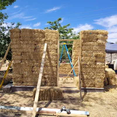 Strawbales stacked to create a square building. The structure is supported with temporary 2x4 bracing. 