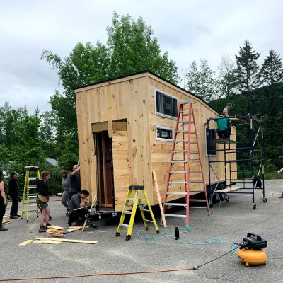 Students working on a tiny house. There are ladders and tools around the building.
