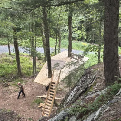A long skinny treehouse platform with a rug and bench on top viewed from above. 