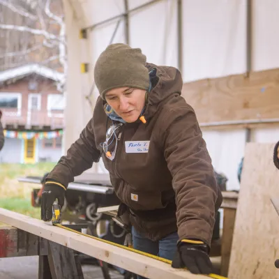 A person takes a measurement on a piece of lumber in an outdoor classroom.