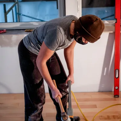 A person using a flooring nailer to install hardwood flooring. 
