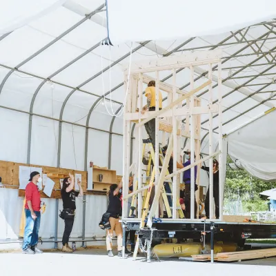 Students work on framing a tiny house on a trailer in an outdoor classroom.